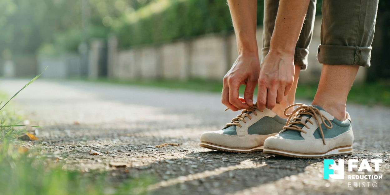 A person’s hands lacing up walking shoes on a sunlit outdoor path, ready for a morning walk