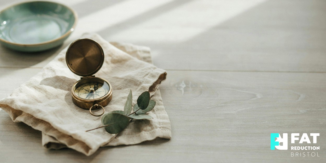 Close-up photograph of a vintage brass compass resting on a folded linen cloth in soft natural daylight